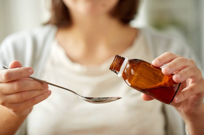 Woman pouring medication or antipyretic syrup from bottle to a spoon.