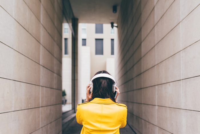 From behind view of young caucasian brown hair woman listening music with headphones - music, technology, relax concept