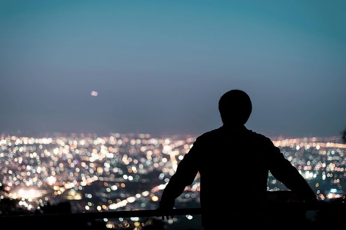 man on a balcony at night staring at city skyline