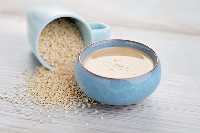 Bowl of tahini next to overturned cup of sesame seeds