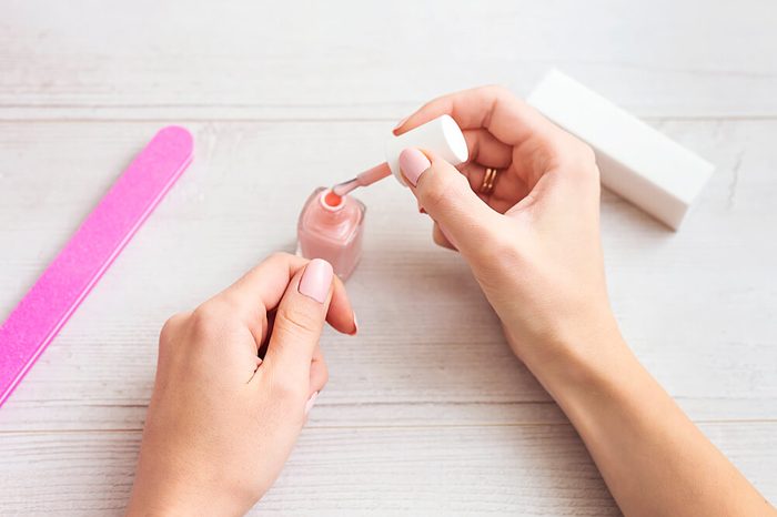 Female hands applying light pink nail polish on wooden table with nail set. Manicure nail paint pink color.