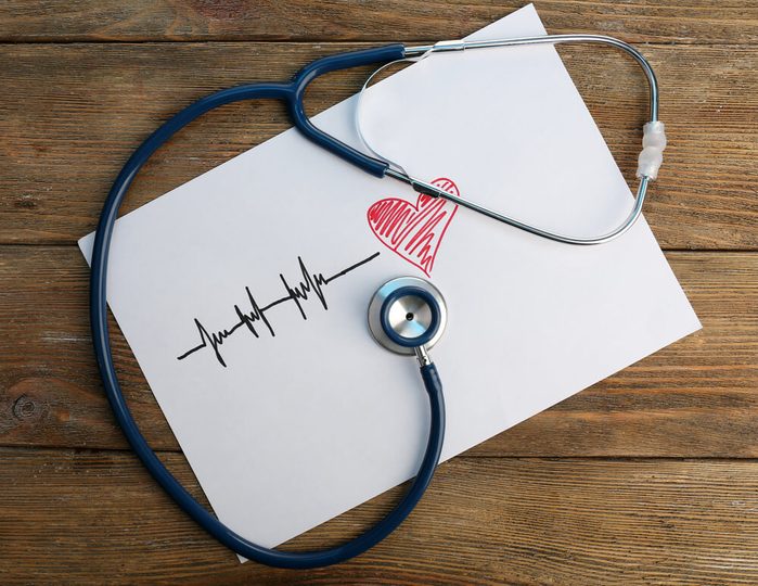 Stethoscope with heart drawing on wooden background