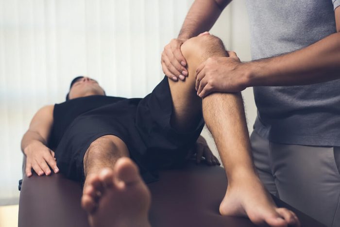 therapist massaging knee of male patient