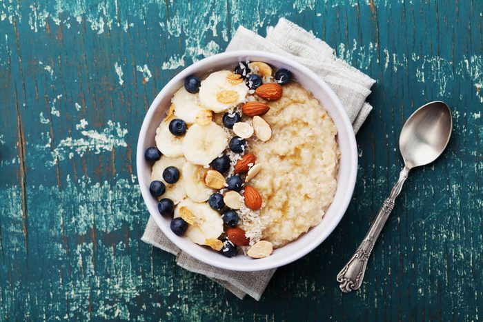 Bowl of oatmeal porridge with banana, blueberries, almonds, coconut and caramel sauce on teal rustic table, hot and healthy food for Breakfast, top view, flat lay