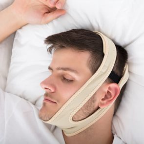 Young Handsome Man Sleeping With Anti Snoring Chin Strap On Head At Home