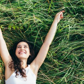 Young happy woman laughing in a bed of grass with arms outstretched