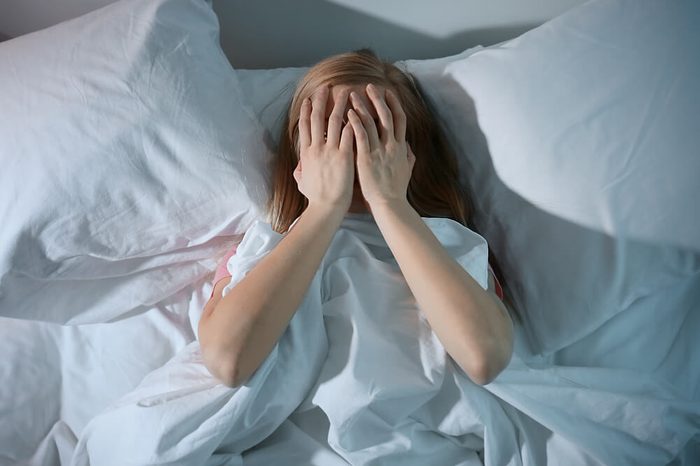Young scared woman lying in bed with her hands over her face