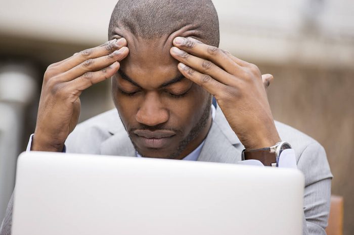 stressed young businessman working on laptop computer holding head with hands looking down.