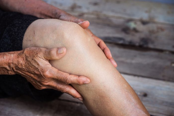 An older person with osteoarthritis holding sore knee