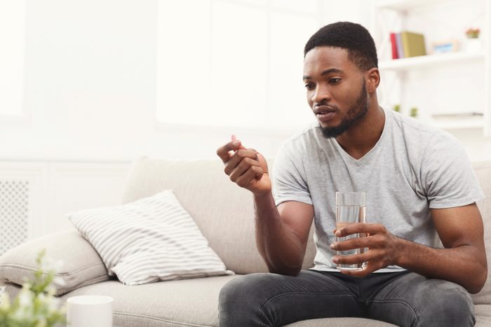 Serious african-american man ready to take a pill while sitting on a couch at home, copy space