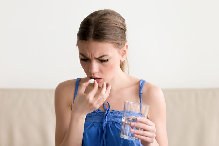 Worried sick young woman holding pill glass of water at home, teen feels ill taking medicine, depressed girl about to take antidepressant pill, emergency contraceptive, painkiller for painful periods