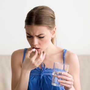 Worried sick young woman holding pill glass of water at home, teen feels ill taking medicine, depressed girl about to take antidepressant pill, emergency contraceptive, painkiller for painful periods