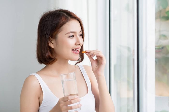 Close Up Of Happy Asian Woman Taking Pill With Omega-3 And Holding A Glass Of Fresh Water In Morning. Vitamin D, E, A Fish Oil Capsules. Nutrition. Healthy Eating, Lifestyle.