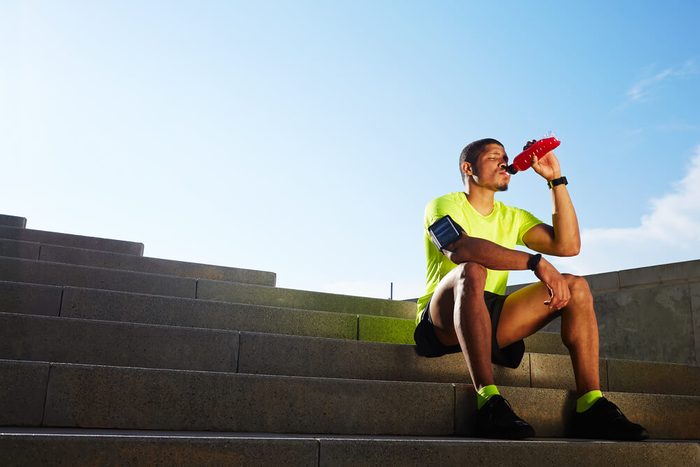 Handsome male runner seated on the steps drink water, beautiful fit man in bright fluorescent sportswear, sports fitness concept