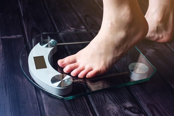 Female feet standing on electronic scales for weight control on wooden background