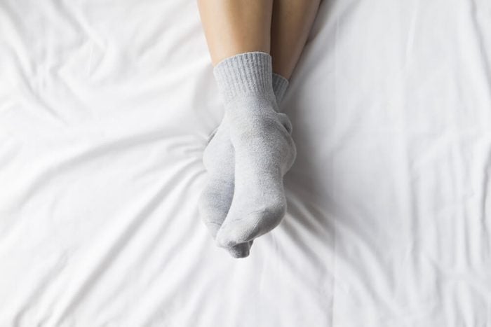 Female feet in warm woolen socks around her feet .Part of the body.Beautiful female legs sitting on the bed. Relax concept.