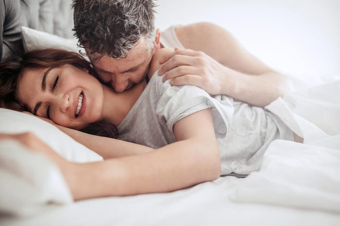Beautiful passionate couple waking up in bed. Man kissing on neck of woman, both lying on bed.