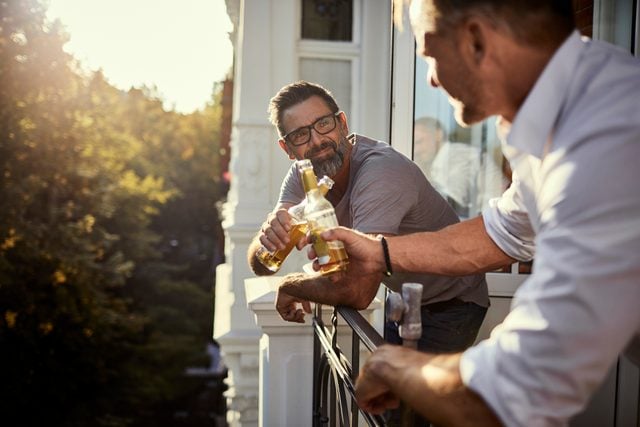 two mature men drinking beer on balcony