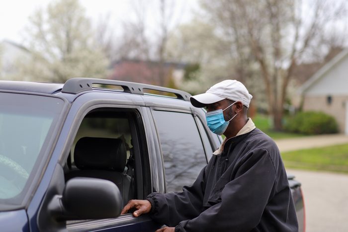 man wearing mask outside getting into car