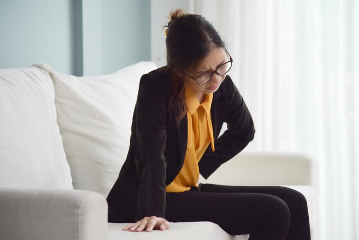 Young Asian glasses business woman sitting on sofa and suffering from stomach ache. Illness, diseases concept.