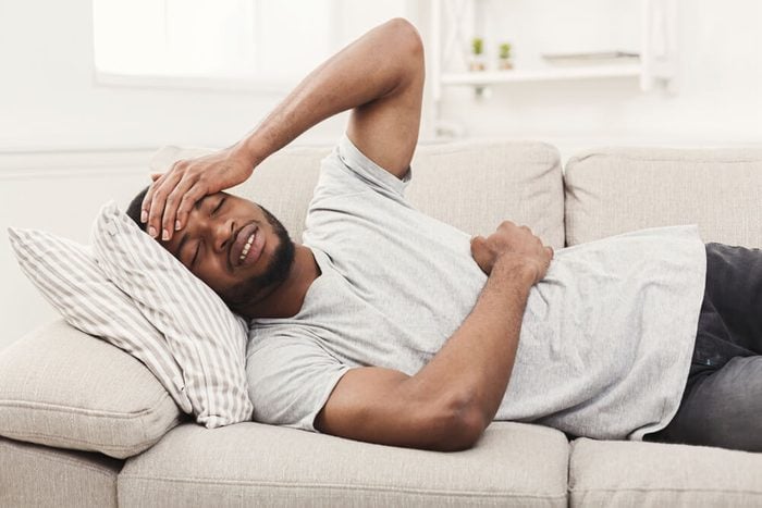 Handsome young african-american man suffering from stomachache and headache, while lying on sofa at home