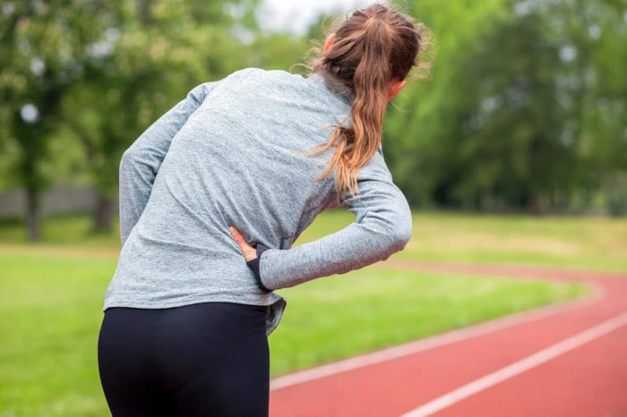 Athletic woman on running track has side cramps during workout