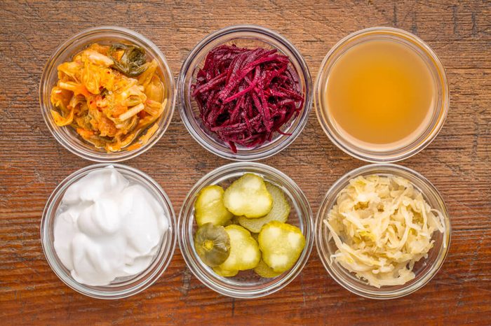 Fermented food great for gut health--glass bowls of kimchi, red beets, apple cider vinegar, coconut milk yogurt, cucumber pickles, sauerkraut