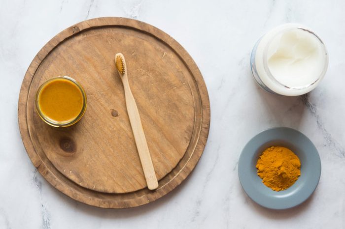 Jar of turmeric spice and toothbrush on a wooden plate.
