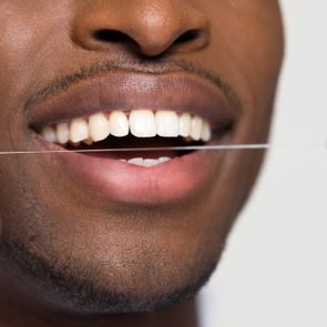 Close up view of african american black man cleaning white healthy teeth holding using dental floss isolated on grey studio blank background, oral hygiene concept, tooth health care caries prevention