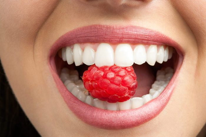 Macro close up of healthy female teeth biting raspberry.