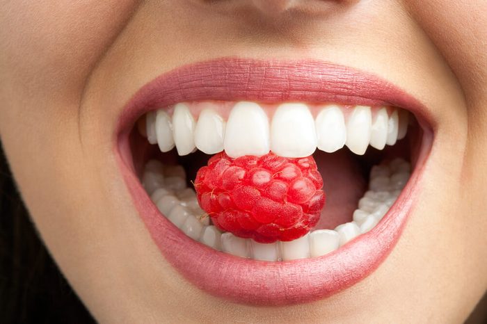 Healthy woman's teeth biting a raspberry.