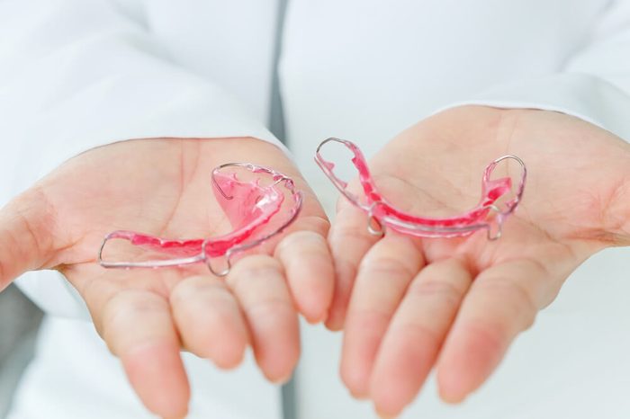 Dentist holding two mouth retainers in each hand.