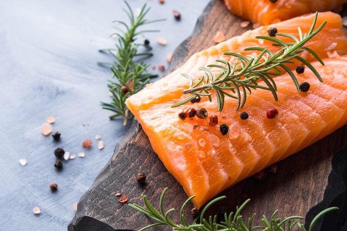 Raw salmon pieces on wooden board with herbs, salt and spices