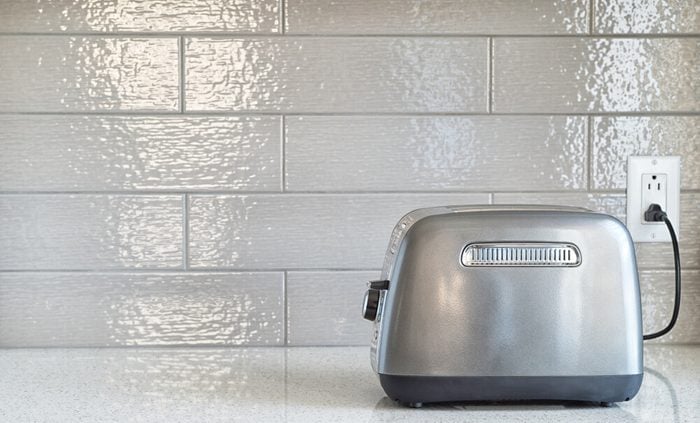 Plugged in retro styled toaster with sliced bread against grey ceramic backsplash in background