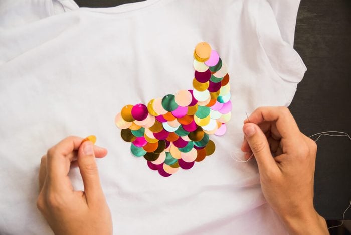 girl decorates white T-shirt with colored sequins for gift