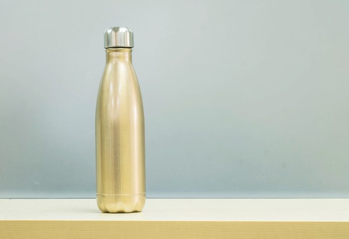 Closeup gold color of aluminium flask for keep hot water on blurred wooden desk