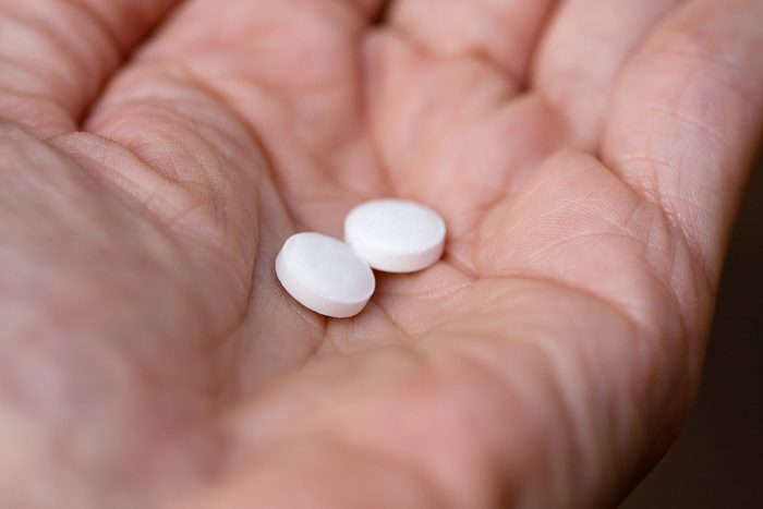 Hand holding two aspirin tablets.