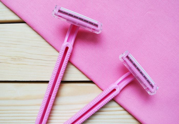 Two pink women's disposable razors on wooden table.
