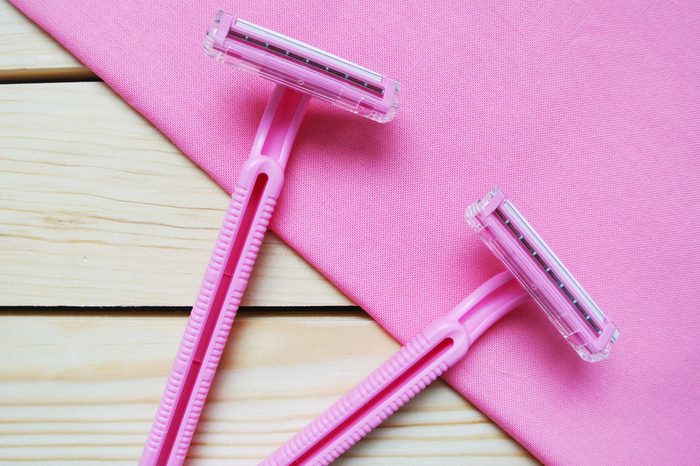 Couple of pink women's disposable razors on wooden table.