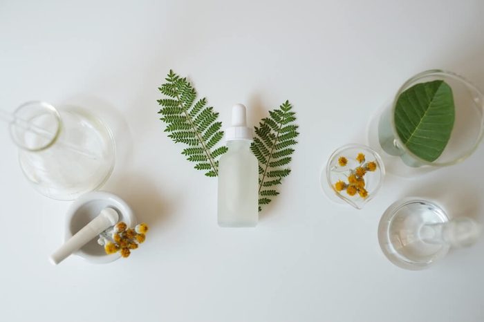 White glass cosmetic bottle with laboratory glassware and leaves