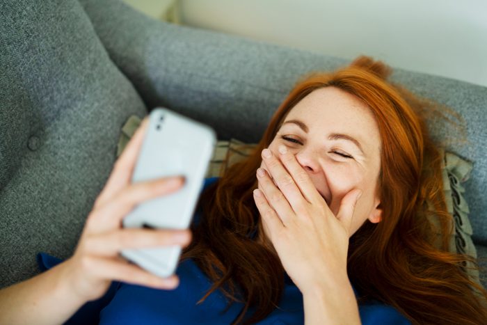 woman lying on couch laughing at phone