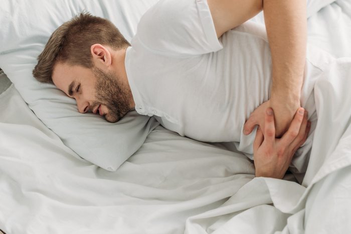 man laying in bed with stomach pain