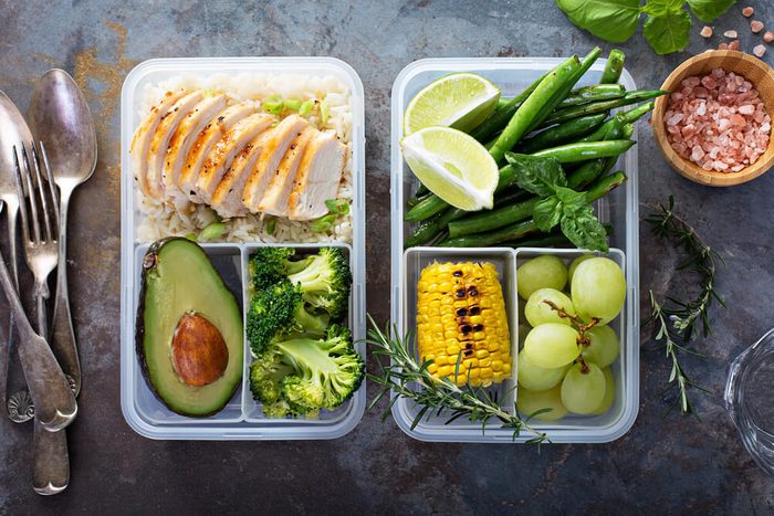 Healthy green meal prep containers with chicken, rice, avocado and vegetables overhead shot