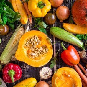 Fresh vegetables on a dark table. Autumn background. Healthy eating. Sliced pumpkin, zucchini, squash, bell peppers, carrots, onions, garlic, tomatoes, eggplant, corn cob, rucola and basil. Top view