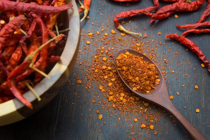 Cayenne pepper on a wooden spoon with bowl of whole peppers