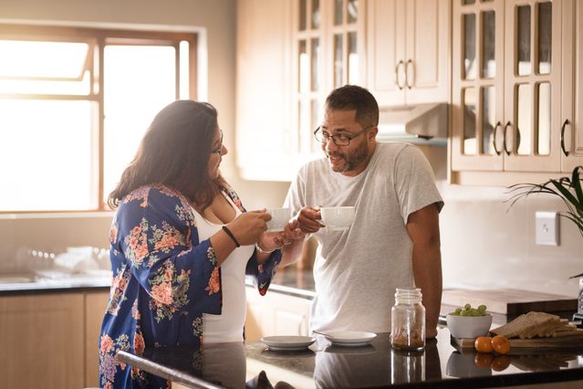 couple standing in kitchen talking and drinking coffee