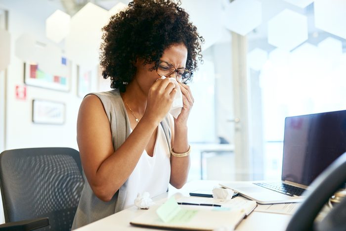 woman sneezing while working at desk