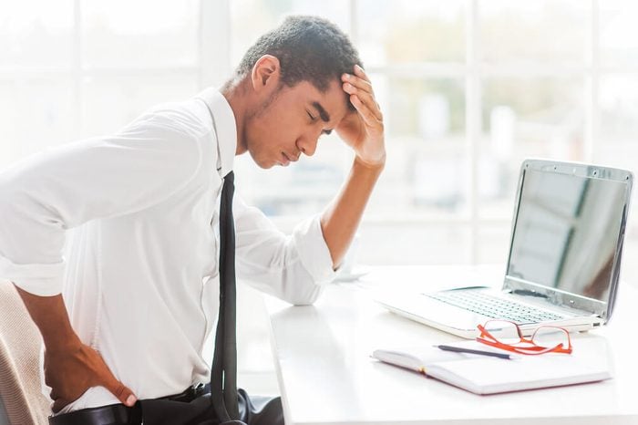 Man sitting at his desk holding his back as if in pain.