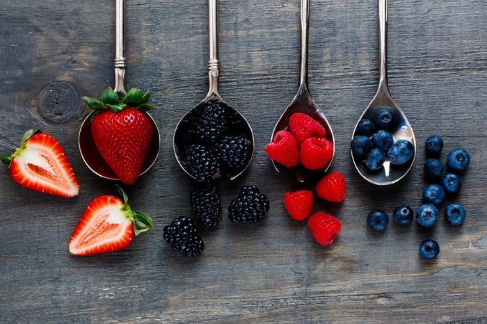 Strawberries, raspberries, blueberries and blackberries on vintage metal spoons over dark wood. Agriculture, Gardening, Harvest Concept. Background with space for text.