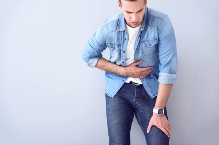 Man in a jean shirt holding his stomach as if having a stomachache.